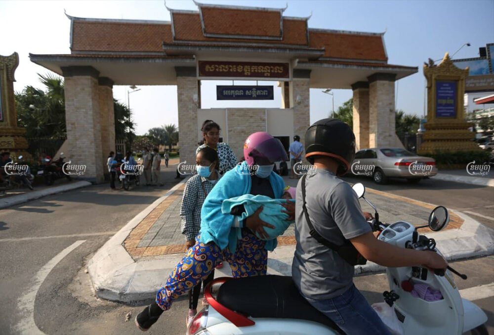 A garment worker carries her son to ride a motorcycle after receiving compensation at the Kandal Provincial Hall on Friday. CamboJA/ Pring Samrang