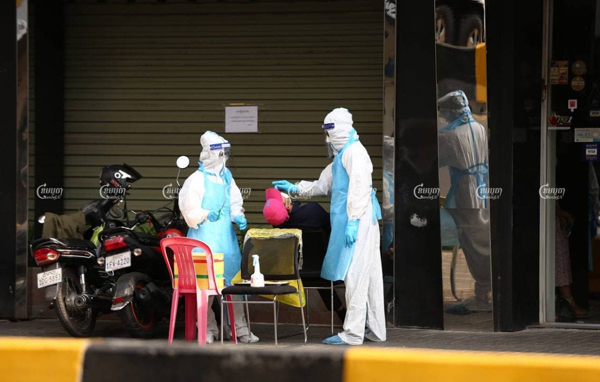 Health workers conduct a COVID-19 test on Monday outside a clothing shop in Phnom Penh. Panha Chhorpoan