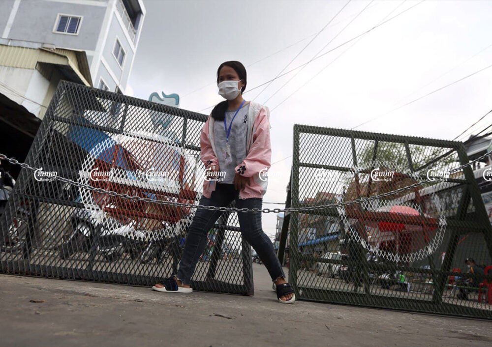 A garment worker crosses a barrier placed at the border of a red zone in Choam Chao 1 commune, Pur Senchey district in Phnom Penh. Picture taken on May 12, 2021. CamboJA/ Pring Samrang