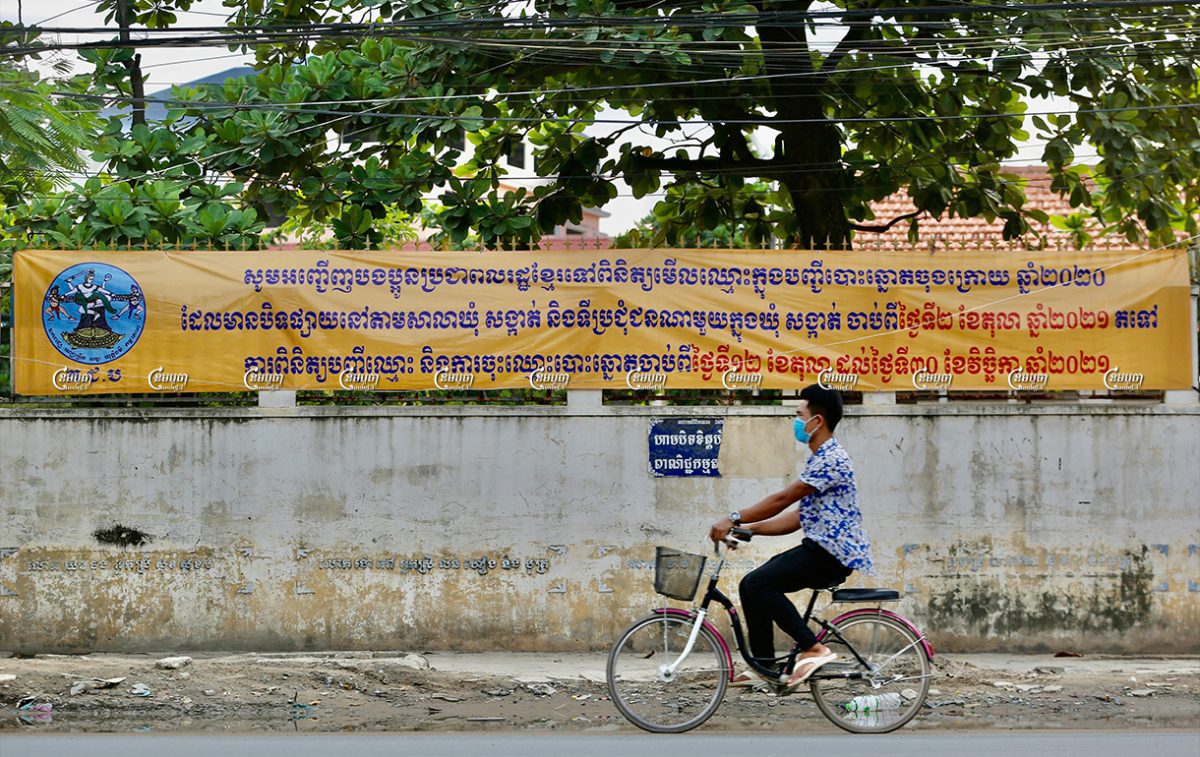 A man rides a bicycle past a banner asking people to confirm their personal information and register to vote ahead of the 2022 commune election, October 4, 2021. CamboJA/ Panha Chhorpoan