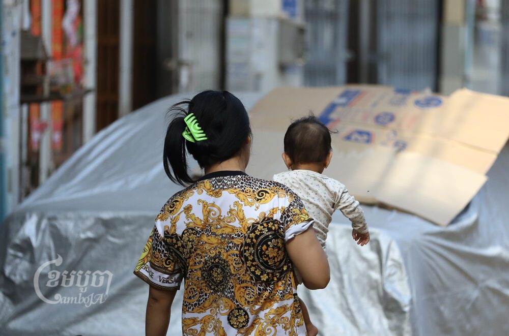 A woman with a baby walks in a village in Phnom Penh, March 30, 2022. CamboJA/Pring Samrang