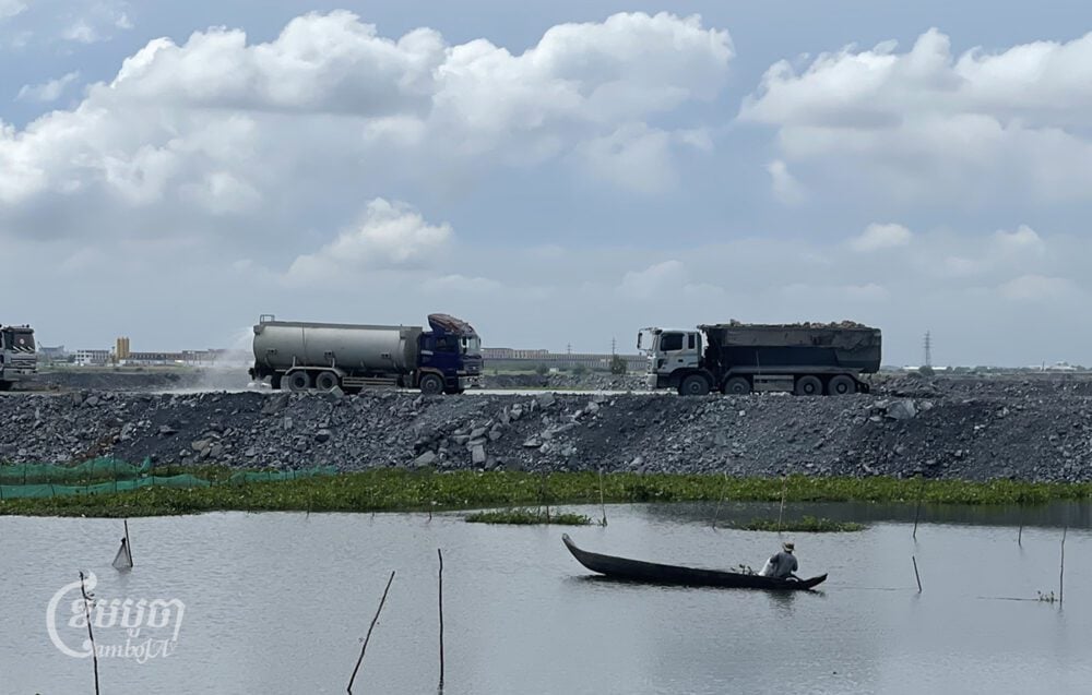 A man catches fish at Boeung Tamok lake while a truck carries soil to fill the lake in Phnom Penh on November 7, 2023. (CamboJA/Pring Samrang)