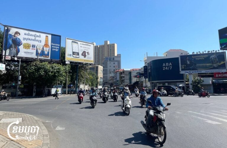 Motorists drive past billboards advertising alcohol products in an intersection in Chamkarmon district, Phnom Penh, December 17, 2024. (CamboJA/ Pring Samrang)