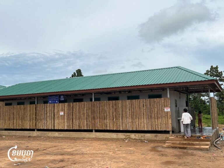 A woman walks into a toilet while a young girl waits for her mother in the bathroom at the 5,000 Bodhi Trees Pagoda displacement camp in Kulen district, Preah Vihear province, on September 13, 2025. (CamboJA/Pa Tongchen)