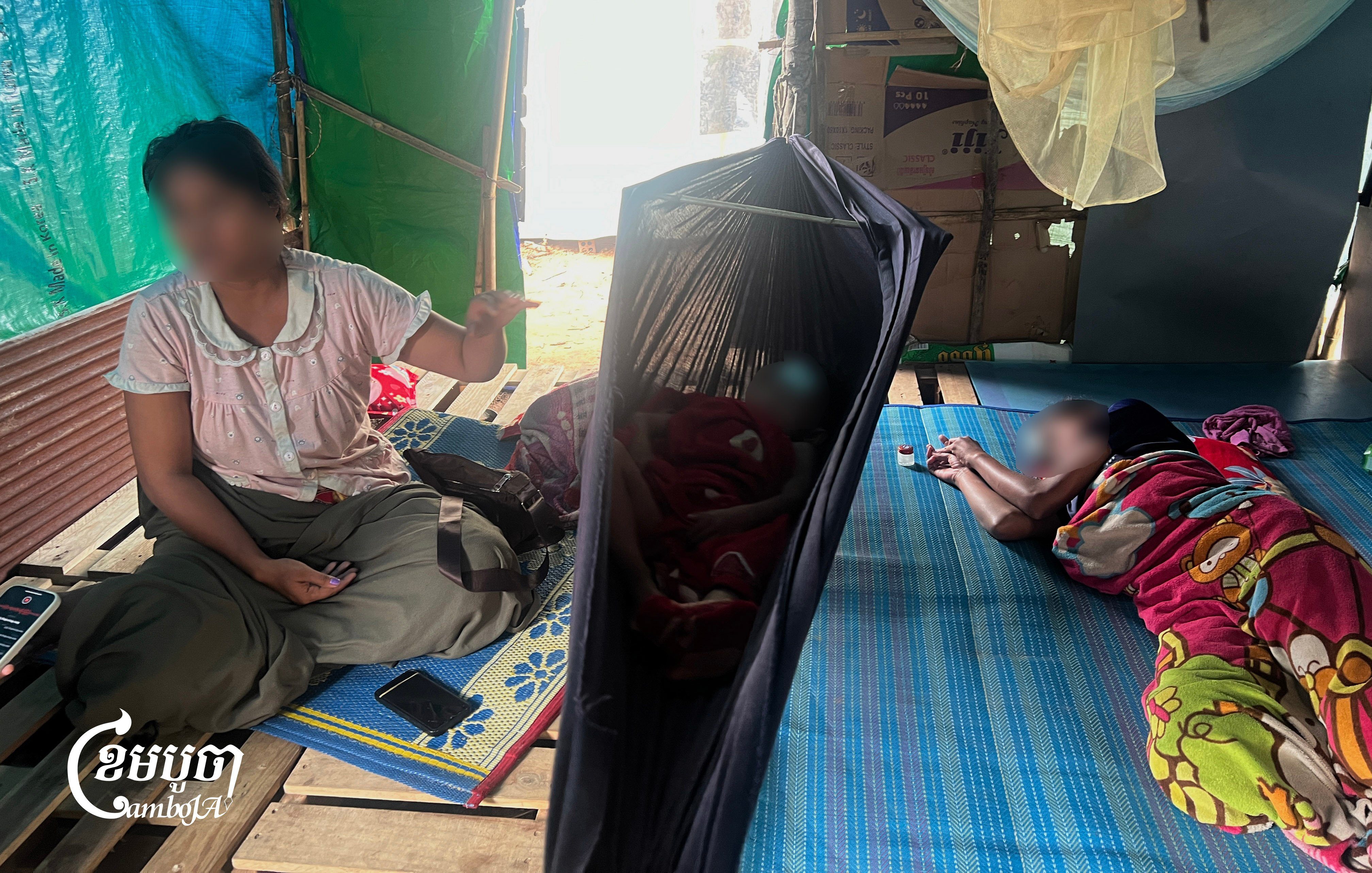 A mother rocks her feverish son to sleep in a cot, while keeping a close watch over her sick daughter nearby, at the Wat Ouddarkiri Tuol Andet displacement camp on September 14, 2025. (CamboJA/Phon Sothyroth)