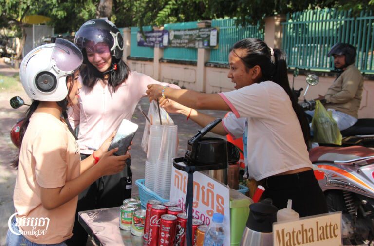 Chan Sophavy, a 24-year-old student, sells packed rice and drinks on the sidewalk in front of Chea Sim Samaky High School on October 23, 2025. (CamboJA/Sea Panha)