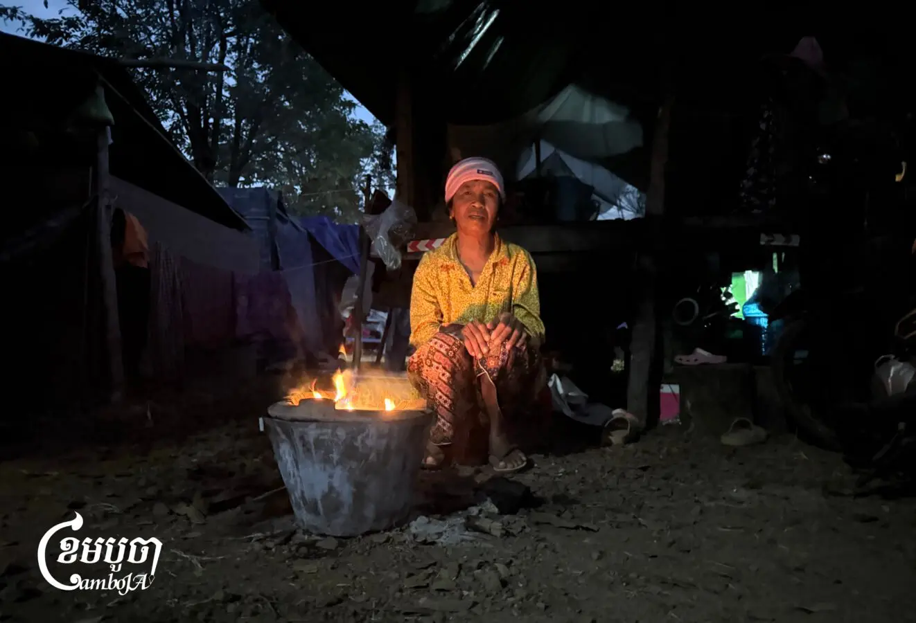 A woman is keeping herself warm by the fire in the early morning at a safe center in Preah Vihear province on December 17, 2025. (CamboJA/Va Sopheanut)